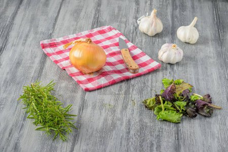 Foto de Una mesa de cocina gris con ajo, una cebolla, un paño de cocina, hojas de ensalada y tomillo - Imagen libre de derechos