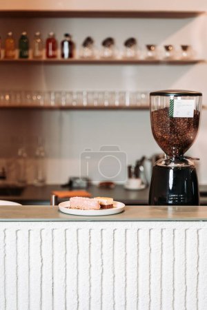 Foto de Un pedazo de pastel en la parte superior brillante de una barra, en un café, con una máquina de puesta a tierra de café, y estantes borrosos con vasos y botellas en el fondo - Imagen libre de derechos