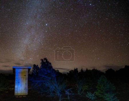 Téléchargez les photos : Une toilette extérieure en bois dans la nature sous un beau ciel étoilé sombre - en image libre de droit