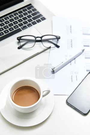 Photo for A vertical top view of a white office table with a notebook, glasses and a cup of coffee - Royalty Free Image