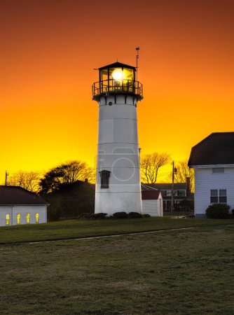Téléchargez les photos : Vue verticale d'un phare parmi les bâtiments ruraux de Chatham, Cape Cod, Massachusetts au coucher du soleil - en image libre de droit