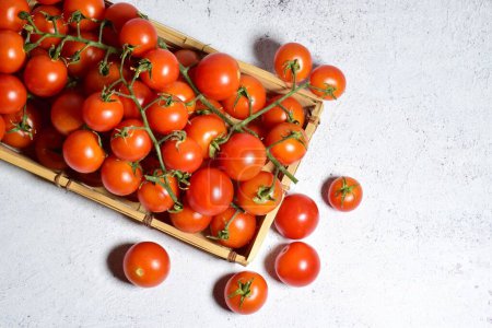 Foto de Una vista superior de tomates cherry jugosos regordetes en bandeja de madera en la superficie de piedra - Imagen libre de derechos