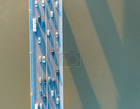Téléchargez les photos : Voitures de ville se déplaçant au pont autoroutier sur fond ensoleillé surface de la rivière, vue sur drone - en image libre de droit