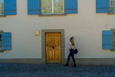 Téléchargez les photos : Une jeune femme blonde passant devant un immeuble aux volets bleus. - en image libre de droit