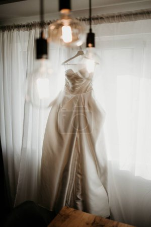 Foto de Una toma vertical del hermoso vestido de novia blanco colgando de la cornisa de la ventana - Imagen libre de derechos