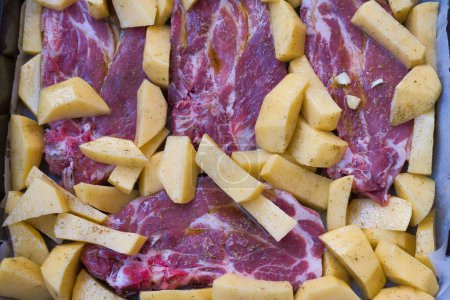 Foto de Comida casera, filetes con papas fritas listos para ir en el horno. Ingredientes filete de cerdo, patatas, sal, aceite, mantequilla, orégano y pimienta - Imagen libre de derechos