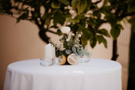Téléchargez les photos : Une petite table avec une nappe blanche et une décoration bouquet-bougie préparée pour une cérémonie de mariage - en image libre de droit