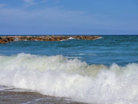 Photo for A beautiful shot from the beach of sea wave and stone barrier behind - Royalty Free Image