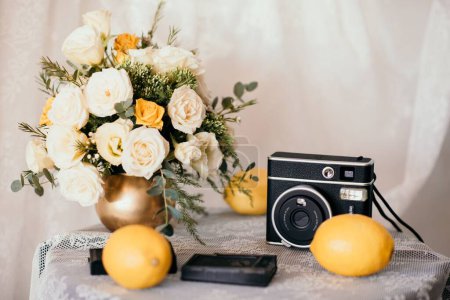 Foto de Un primer plano de una pequeña mesa decorada con un ramo de flores, una cámara y limones - Imagen libre de derechos
