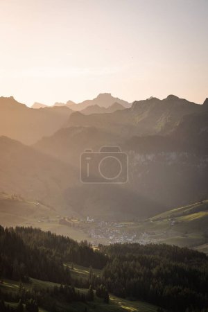 Téléchargez les photos : Vue verticale d'une belle petite ville dans une vallée verdoyante avec une chaîne de montagnes et une forêt de pins en arrière-plan au lever du soleil - en image libre de droit
