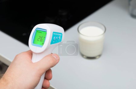 Téléchargez les photos : Un gros plan d'un thermomètre infrarouge médical sans contact mesurant la température du lait maternel - en image libre de droit