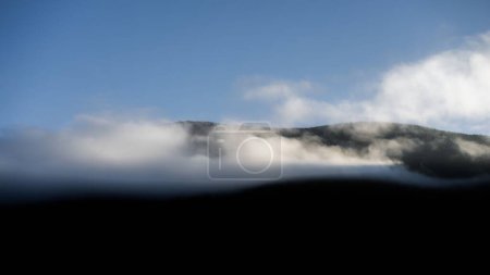 Photo for The blue sky over the silhouetted hills barely seen through the dense fog - Royalty Free Image