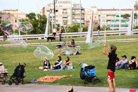 Téléchargez les photos : Un mec souffle des bulles de savon dans un parc avec des gens en arrière-plan, Barcelone, Espagne - en image libre de droit