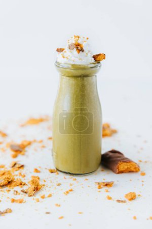 Photo for A vertical closeup shot of a glass of green smoothie with whipped cream on it on a white surface - Royalty Free Image