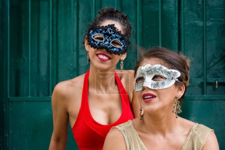Foto de Un selectivo de dos hembras con máscaras de carnaval en ropa ligera de verano contra una puerta de color verde - Imagen libre de derechos