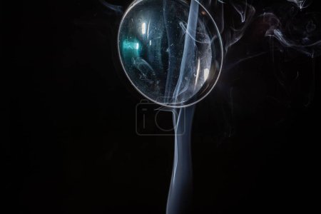 Photo for A closeup of a magnifying glass against a black background and smoke coming from below - Royalty Free Image