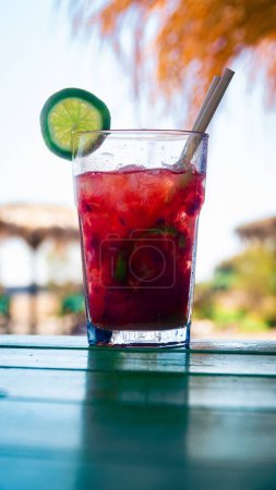 Photo for A vertical shot of a bright rec iced cocktail with lime and a straw - Royalty Free Image