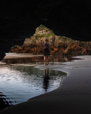Téléchargez les photos : Un plan vertical de la fille espagnole par derrière debout sur la plage visible à travers les rochers - en image libre de droit