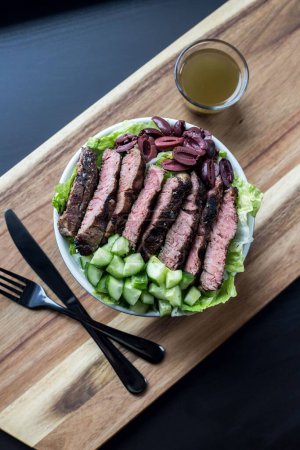 Photo for A vertical top view shot of the steak salad on a white plate with a sauce on a wooden board - Royalty Free Image