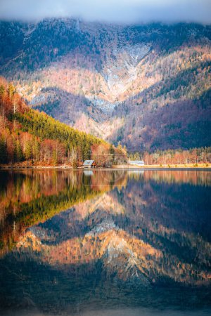Téléchargez les photos : Plan vertical d'un lac reflétant les couleurs des arbres d'automne et d'une haute montagne couverte de brouillard - en image libre de droit