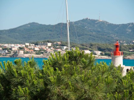Photo for A view from behind green bush of a lighthouse on the Mediterranean and mountain in the background - Royalty Free Image