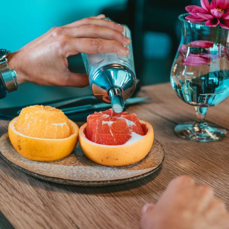 Téléchargez les photos : La main versant du sucre sur le pamplemousse et l'orange - décoration aux fruits - en image libre de droit
