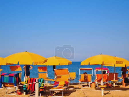 Foto de Un primer plano de sombrillas de playa de color amarillo brillante y gente relajándose frente al mar azul - Imagen libre de derechos
