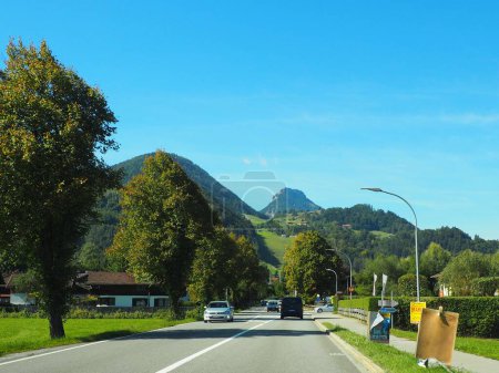 Foto de Una hermosa vista de una carretera con coches y árboles con colinas y un cielo azul en el fondo en Rosenheim - Imagen libre de derechos