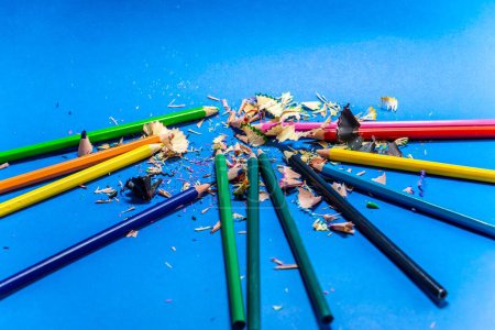 Photo for A closeup of colored pencils isolated on blue background with scraps - Royalty Free Image