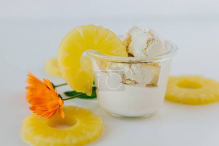 Téléchargez les photos : Gros plan d'un verre de crème glacée entouré d'ananas tranchés et d'une fleur d'orange - en image libre de droit