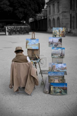 Foto de Un plano vertical de un artista callejero francés en Versalles, sentado en una silla a lo largo de sus pinturas - Imagen libre de derechos