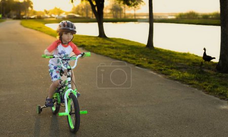 Photo for A cute child boy riding a bike on the river bank wearing a helmet - Royalty Free Image