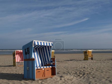 Téléchargez les photos : Chaises de plage à capuchon colorées, sur la plage de sable de l'île Langeoog en mer du Nord, par une journée nuageuse avec vue sur la mer en arrière-plan - en image libre de droit