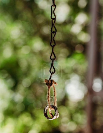 Photo for A vertical shot the wedding rings hanging on the metal chain outside - Royalty Free Image
