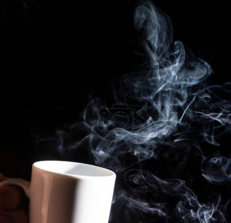 Foto de Un primer plano de una taza blanca sobre un fondo negro con humo saliendo de ella - Imagen libre de derechos
