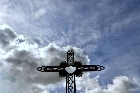 Foto de Un disparo de ángulo bajo de una cruz de metal negro bajo el cielo azul nublado - Imagen libre de derechos