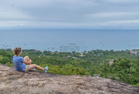 Foto de Espalda de turista mujer sentada en mirador vela roca observando en hermosa vista del paisaje marino con cielo azul claro en Koh Tao, Tailandia. - Imagen libre de derechos