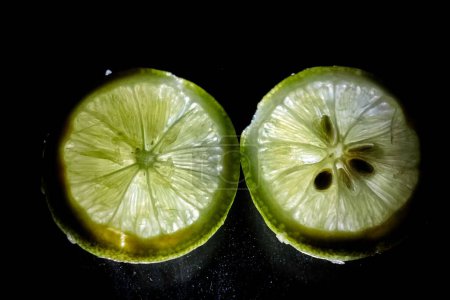 Téléchargez les photos : Plan rapproché de deux tranches de citron vert isolées sur un fond noir - en image libre de droit