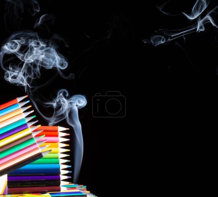 Photo for A closeup of colored pencils grouped on black background with white smoke coming from below, with copy space - Royalty Free Image