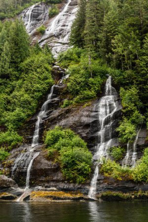 Foto de Una hermosa vista de las cascadas que fluyen por las rocas rodeadas de exuberante vegetación en Misty Fjords, Alaska - Imagen libre de derechos