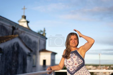 Foto de A woman on the porch of her house looking at the camera against the sky and church in the background - Imagen libre de derechos