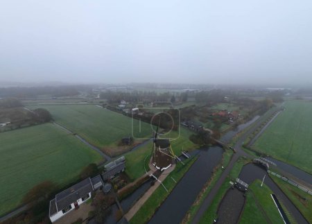 Téléchargez les photos : Une vue aérienne du moulin à vent dans une campagne verdoyante avec des ruisseaux par une journée brumeuse - en image libre de droit