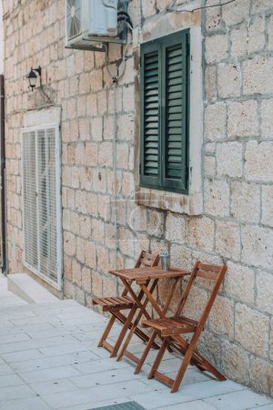 Foto de Un plano vertical de una pared de piedra de una casa y una mesa plegable de madera frente a ella - Imagen libre de derechos