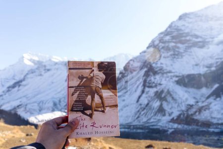 Téléchargez les photos : Un gros plan de la main d'une personne tenant un livre de coureur de cerf-volant contre une énorme montagne - en image libre de droit