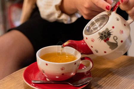 Téléchargez les photos : Gros plan d'une femelle versant du thé dans une belle tasse sur un fond isolé - en image libre de droit