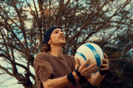 Foto de Un primer plano de un hombre sosteniendo una pelota de fútbol contra los árboles - Imagen libre de derechos