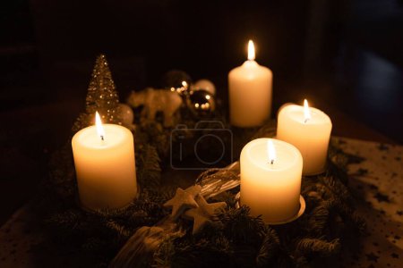 Photo for A closeup shot of burning candles on a wooden table, with a Christmas tree in the background - Royalty Free Image