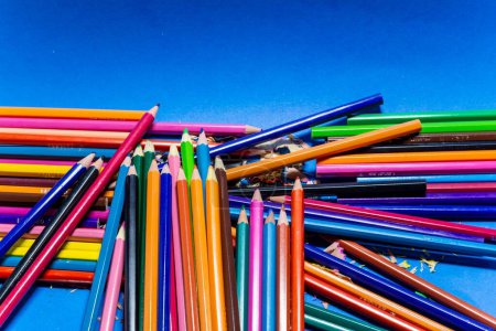 Téléchargez les photos : Un gros plan de pile de crayons de bois colorés et de restes aiguisés isolés sur fond bleu - en image libre de droit