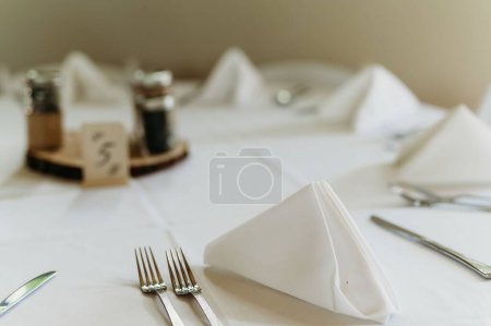 Foto de Los tenedores de plata y cuchillos en una mesa con una cubierta blanca y una bandeja de madera con frascos de vidrio en ella - Imagen libre de derechos