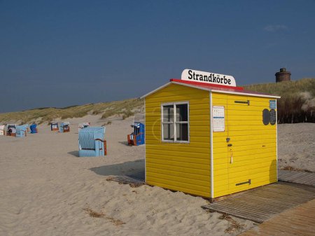 Les chaises de plage à capuchon colorées et une cabane de plage jaune, sur la plage de sable de l'île Juist, par une journée nuageuse, avec une colline herbeuse en arrière-plan